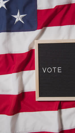 Vertical-Video-Of-Sign-Reading-Vote-Lying-On-US-Stars-And-Stripes-Flag-For-American-Election-2024-3